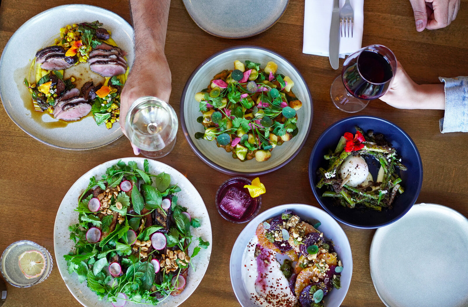 Shared table at Part and Parcel with grain bowls, salads and a glass of red wine
